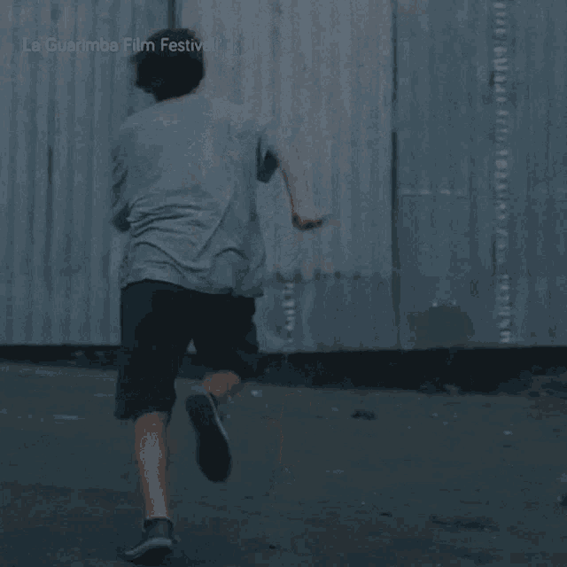 a young boy is running in front of a wooden wall with la guarimba film festival written on it