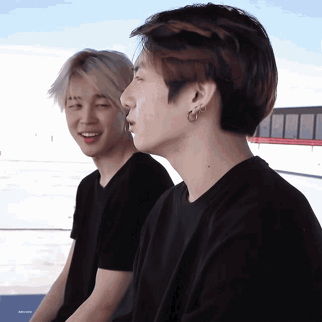 two young men wearing black shirts are sitting next to each other and one of them has a piercing in his ear