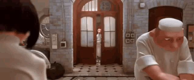 a man and a woman are standing in front of a door in a kitchen .