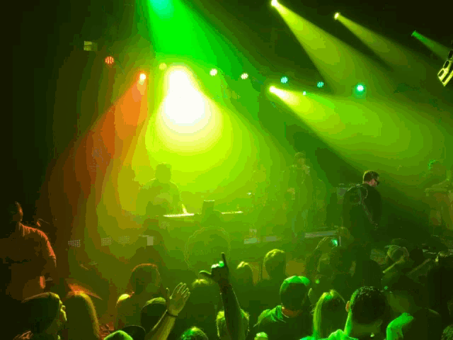 a crowd of people are watching a band on stage with green lights