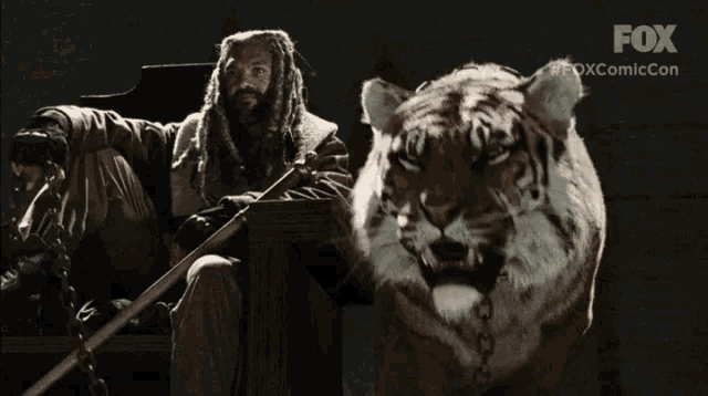 a man is sitting next to a tiger with the fox logo behind him