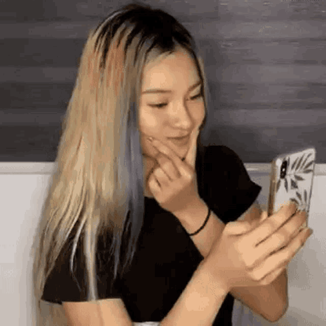 a woman is looking at her phone and smiling while holding her hand to her face .