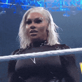 a woman with blonde hair is standing in a wrestling ring with the letter v on her chest
