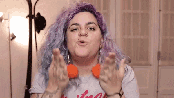a woman with purple hair and orange earrings is blowing a kiss