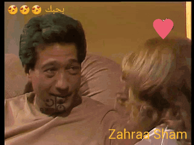 a man and a woman are sitting on a couch with zahraa sham in the corner
