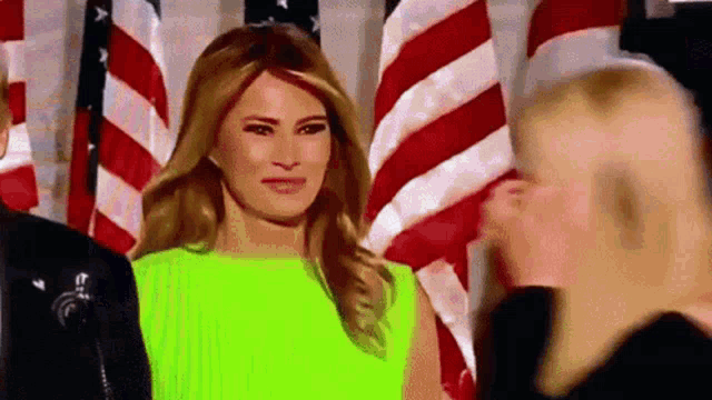 a woman in a neon green dress is standing in front of a group of american flags .