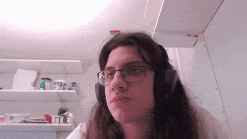 a woman wearing glasses and headphones looks at the camera in a kitchen