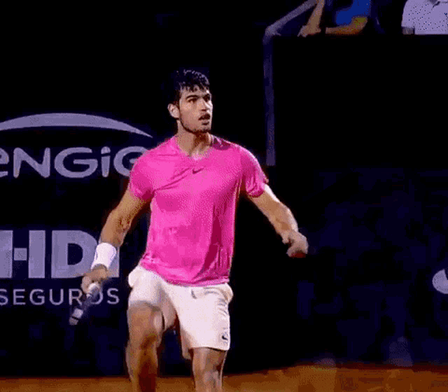 a man in a pink shirt and white shorts is holding a tennis racquet ..