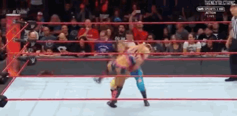 two wrestlers are fighting in a wrestling ring while a referee looks on .