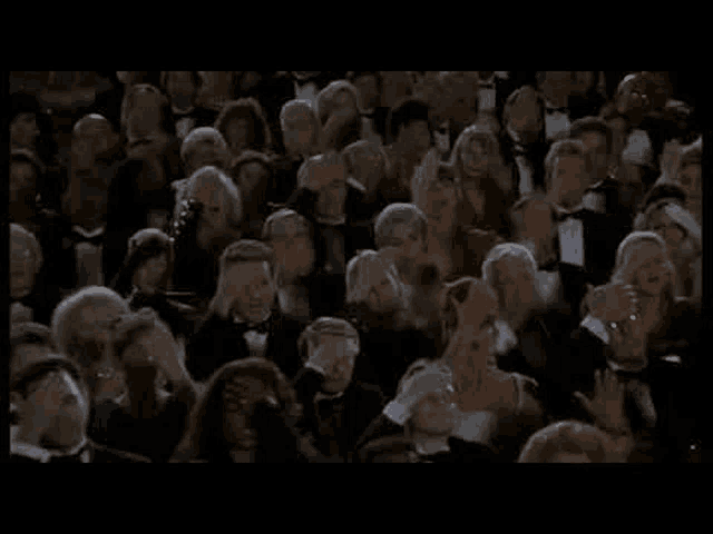 a crowd of people in tuxedos are clapping their hands in a theater .