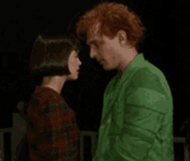 a man in a green jacket and a woman in a red dress are looking at each other .