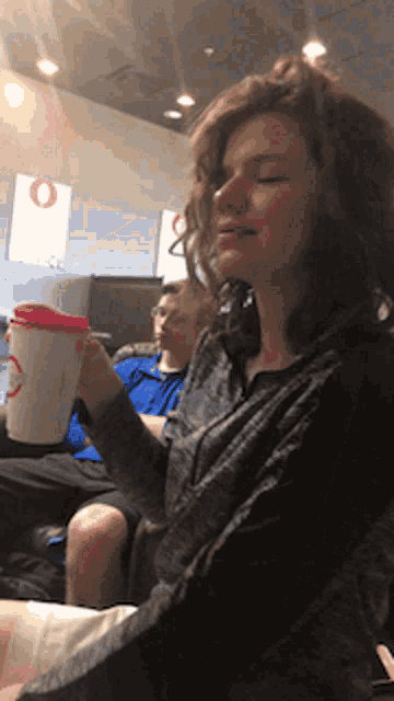 a woman holding a cup with a red lid that says ' o ' on it