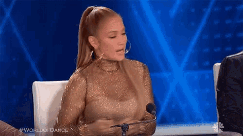 a woman in a gold dress is sitting at a table with a microphone .