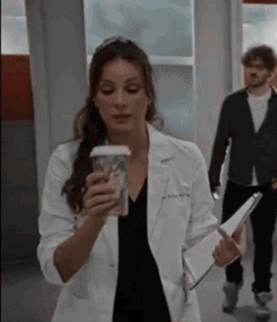 a woman in a white lab coat is holding a cup of coffee