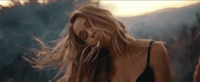 a woman with long blonde hair is standing in front of a mountain .