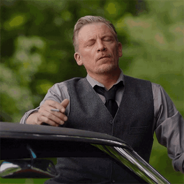 a man in a vest and tie is smoking a cigarette