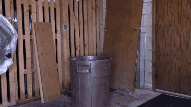 a trash can sits in front of a wooden wall