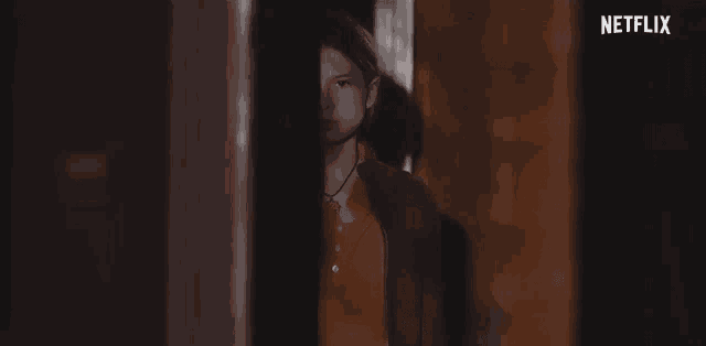 a girl in an orange shirt is standing in a doorway in a dark room .