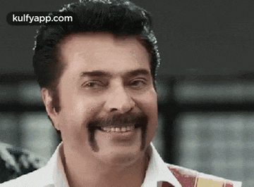 a man with a mustache is smiling in a close up of his face .