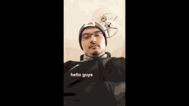 a man wearing glasses , a beanie , and a black jacket is looking at the camera .