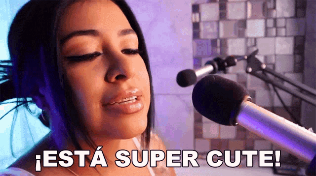 a woman is singing into a microphone with the words " esta super cute " below her