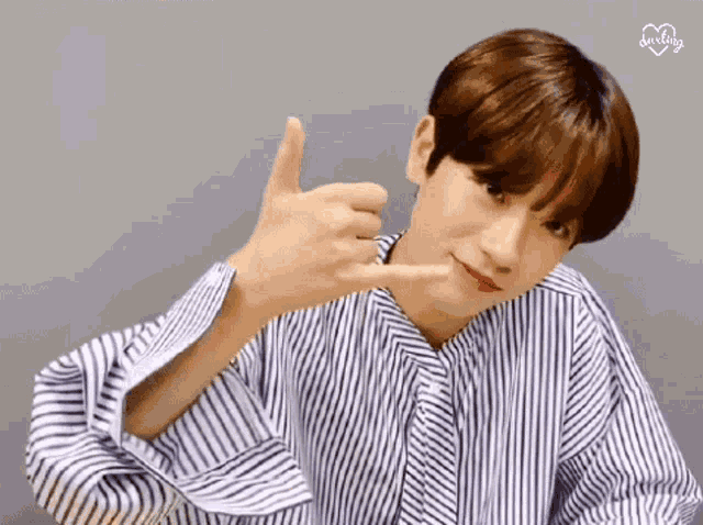a young man in a striped shirt is making a call me sign with his hands .