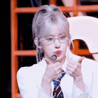 a young woman wearing glasses and a tie is giving a thumbs up .