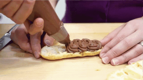 a person is piping chocolate frosting on a pastry on a cutting board