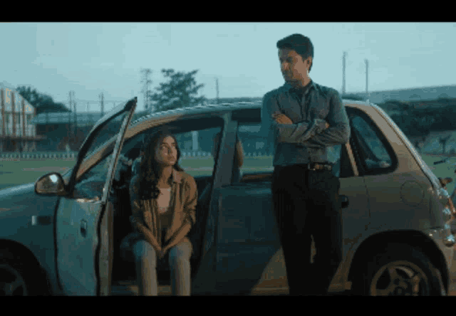 a man and woman standing next to a car with the door open