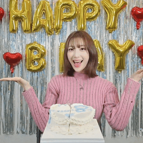 a woman in a pink sweater is holding a cake in front of a happy birthday backdrop