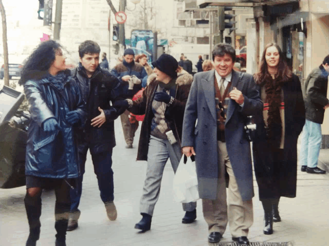 a group of people are walking down a street and one of them is wearing a black hat