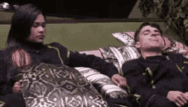 a man and a woman are laying on a couch with pillows