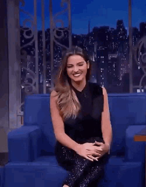 a woman is sitting on a blue couch with her legs crossed and smiling