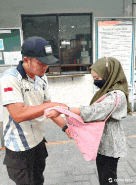 a man giving a woman a pink towel in front of a sign that says " inklusi k3 untuk tenaga kerja "