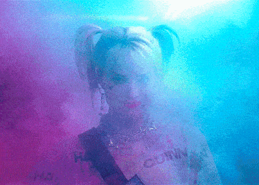 a woman in a harley quinn costume is surrounded by smoke in a dark room .