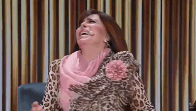 a woman in a leopard print shirt is sitting in front of a curtain and laughing .