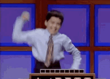 a man in a shirt and tie is standing in front of a podium with his arms in the air .