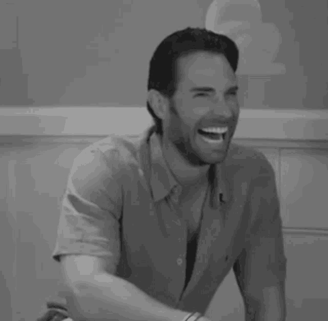 a black and white photo of a man laughing while sitting at a table .