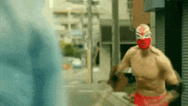 a shirtless man wearing a red mask is running down a city street .