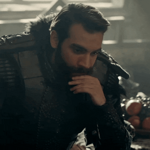a man with a beard is sitting in a chair with his hand to his mouth