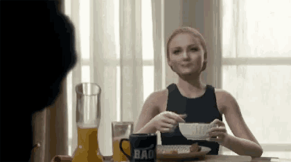 a woman sits at a table with a cup that says bad on it