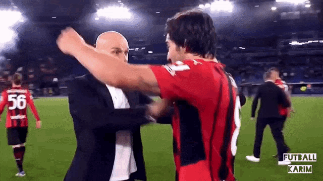 a man in a suit is hugging a man in a red shirt with the number 56 on it