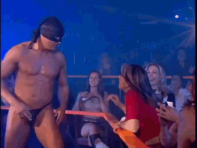 a shirtless man in a mask is being touched by a woman in a crowd .