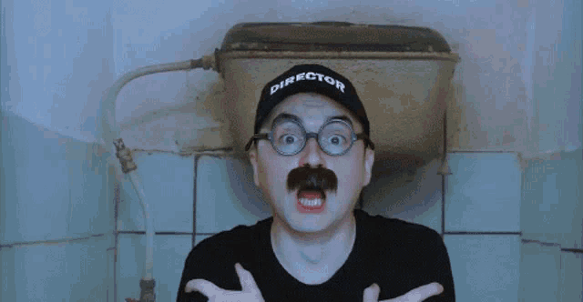 a man with a mustache and glasses wears a hat that says director