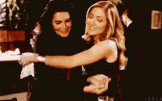 two women are hugging each other in a dark room while sitting at a table .