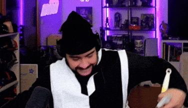 a man with a beard wearing a black hat and a white vest is dancing in a room .