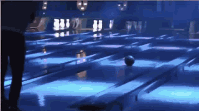 a bowling alley is lit up with blue lights and a bowling ball is on the lane .