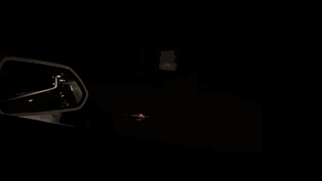 a red car is driving down a street at night with its headlights on