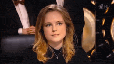 a young woman wearing a necklace and a black shirt is sitting in front of a crowd .