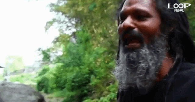 a man with dreadlocks and a beard is standing in front of trees .